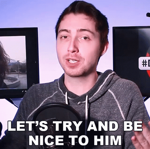 A Man Speaking Into A Microphone With The Words " Let 'S Try And Be Nice To Him " Above Him GIF