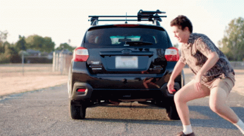 A Man Squats In Front Of A Black Subaru GIF