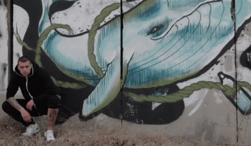 A Man Squatting In Front Of A Mural Of A Whale With The Letter K Visible GIF