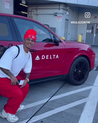A Man Squatting In Front Of A Red Car That Says Delta GIF