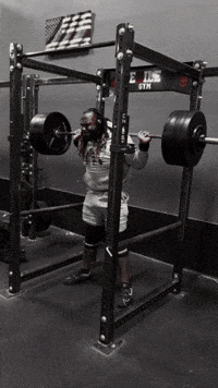 A Man Squatting With A Barbell In Front Of A Rack That Says Evils Gym GIF