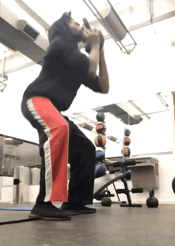 A Man Squatting With A Dumbbell In His Mouth GIF