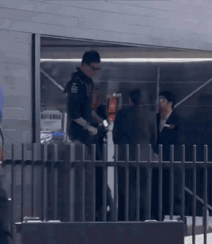 A Man Standing Behind A Fence Talking To A Man In A Suit GIF