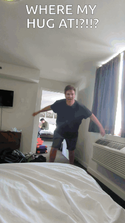 A Man Standing In A Hotel Room With The Words " Where My Hug At " On The Bottom GIF