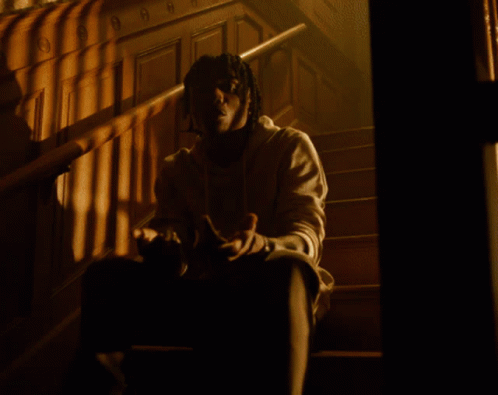 A Man Standing In A Room With White Curtains And A Necklace With The Letter O On It GIF
