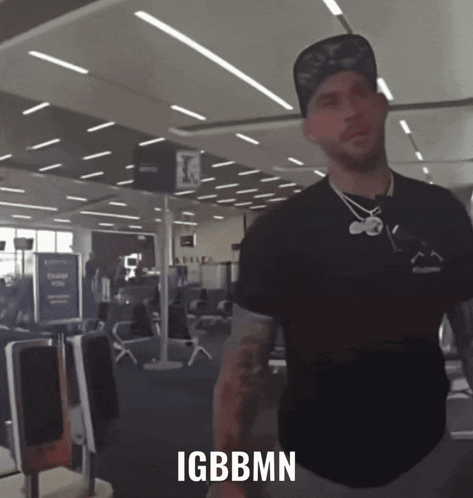 A Man Standing In An Airport With Igbbmn Written On The Bottom Of His Shirt GIF