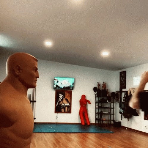 A Man Standing In Front Of A Boxing Dummy In A Room GIF