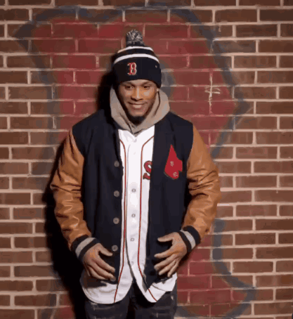 A Man Standing In Front Of A Brick Wall Wearing A Hat With The Letter B On It GIF