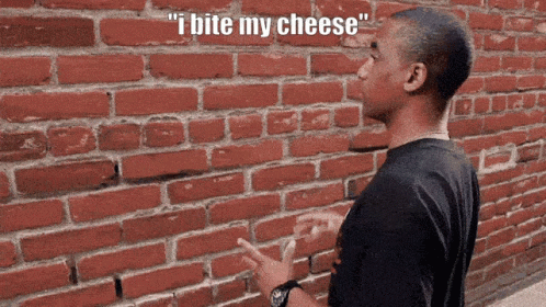 a man standing in front of a brick wall with the words " i bite my cheese " above him