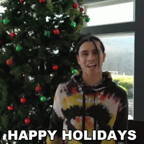 A Man Standing In Front Of A Christmas Tree With The Words Happy Holidays On The Bottom GIF