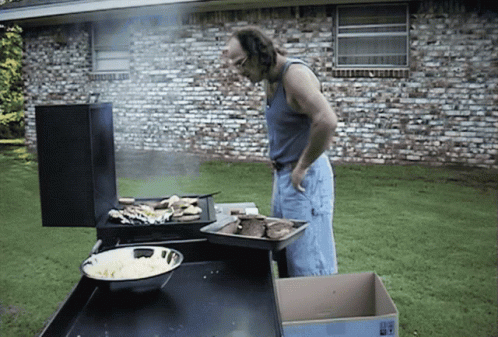 A Man Standing In Front Of A Grill With A Box In Front Of Him That Says " Fragile " GIF