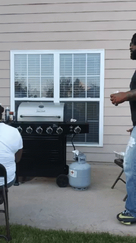 A Man Standing In Front Of A Grill With A Propane Tank In Front Of Him GIF