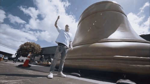 A Man Standing In Front Of A Large Bell With His Hand In The Air GIF