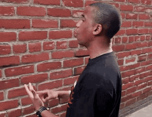 A Man Standing In Front Of A Red Brick Wall GIF