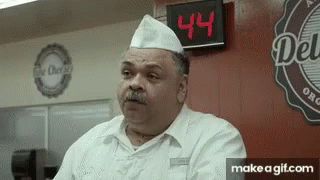 A Man Standing In Front Of A Sign That Says Deli GIF