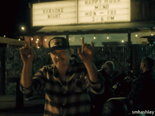 A Man Standing In Front Of A Sign That Says Happy Hour Menu GIF