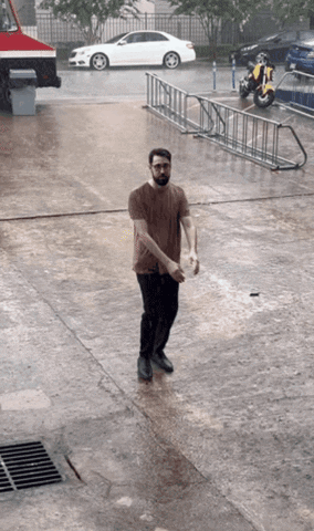 A Man Standing In The Rain With A Motorcycle Parked Behind Him GIF