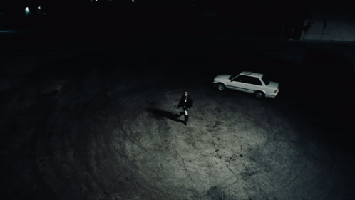 A Man Standing Next To A White Car In A Dark Parking Lot GIF