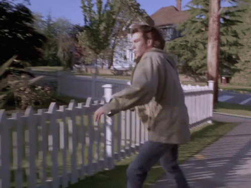 A Man Standing Next To A White Picket Fence Looking Over It GIF