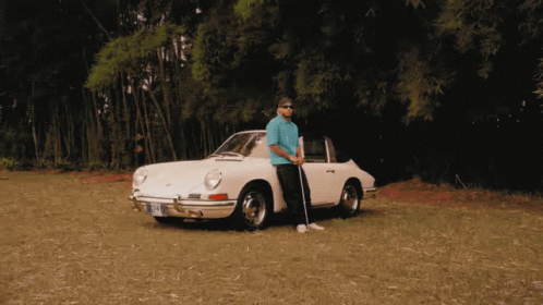 A Man Standing Next To A White Porsche With A Golf Club In His Hand GIF