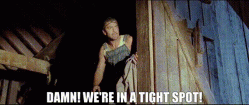 A Man Standing Next To A Wooden Wall With The Words Damn We 'Re In A Tight Spot . GIF