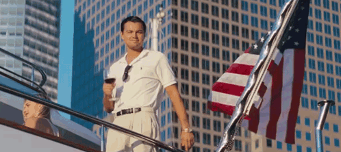 A Man Standing On A Boat Holding A Glass Of Wine In Front Of An American Flag GIF