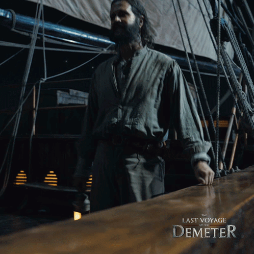 A Man Standing On A Boat With The Last Voyage Of Demeter Written On It GIF