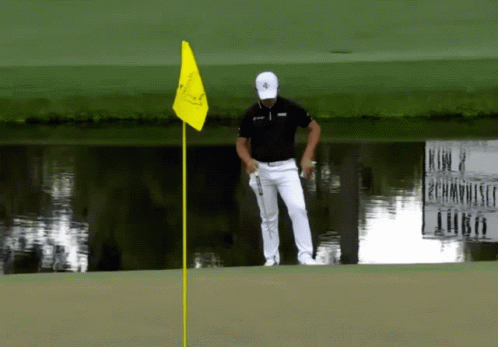 A Man Standing On A Golf Course With A Yellow Flag GIF