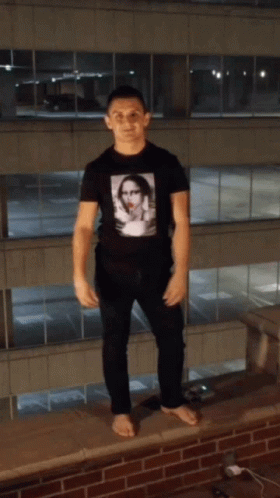 A Man Standing On A Ledge With His Arms Up GIF