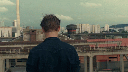 A Man Standing On A Rooftop Looking At A City GIF