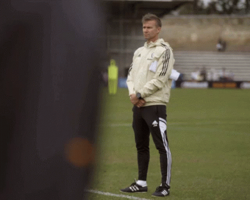 a man standing on a soccer field wearing adidas pants