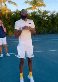 A Man Standing On A Tennis Court With Tennis Balls Around His Legs GIF