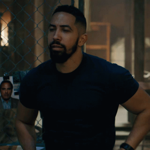 A Man Standing With His Arms Crossed In Front Of A Chain Link Fence GIF