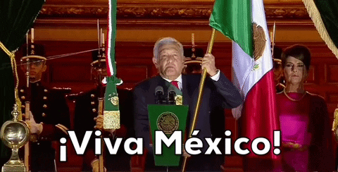 a man stands at a podium holding a mexican flag with the words viva mexico above him