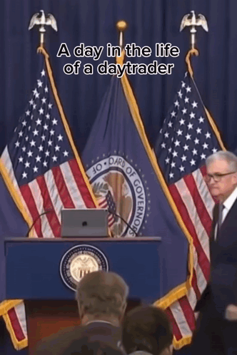 A Man Stands At A Podium In Front Of An American Flag With The Words A Day In The Life Of A Daytrader Above Him GIF
