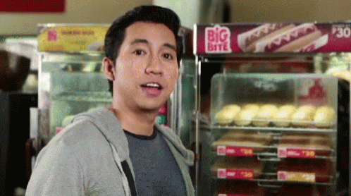 A Man Stands In Front Of A Big Bite Hot Dog Display GIF
