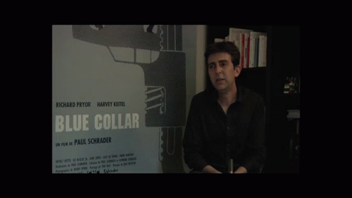 A Man Stands In Front Of A Blue Collar Poster GIF