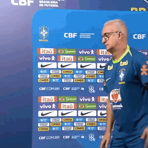a man stands in front of a blue wall with logos for itau and vivo