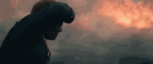 A Man Stands In Front Of A Cloudy Sky With A Sunset In The Background GIF