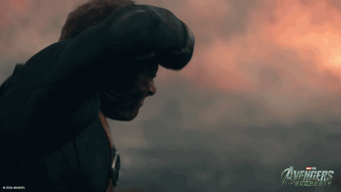 A Man Stands In Front Of A Cloudy Sky With The Avengers Logo On The Bottom GIF