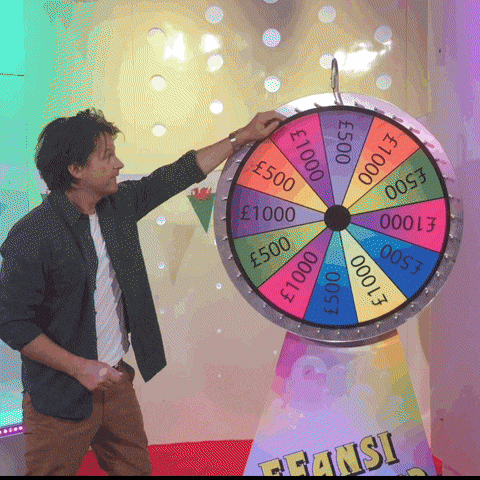 A Man Stands In Front Of A Colorful Spinning Wheel That Says ' Fransi ' On It GIF