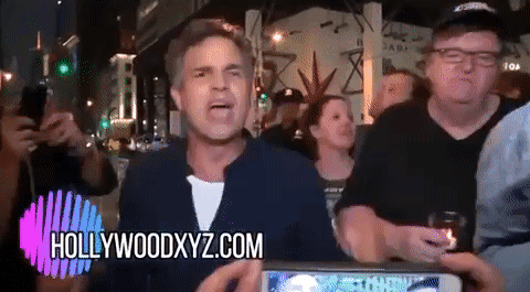 A Man Stands In Front Of A Crowd With Hollywoodxyz.com On The Bottom Right GIF