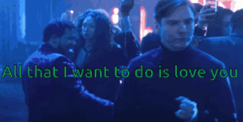 A Man Stands In Front Of A Crowd With The Words " All That I Want To Do Is Love You " Above Him GIF