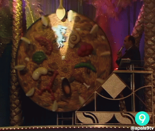 A Man Stands In Front Of A Giant Pizza With The Number 9 On The Bottom GIF