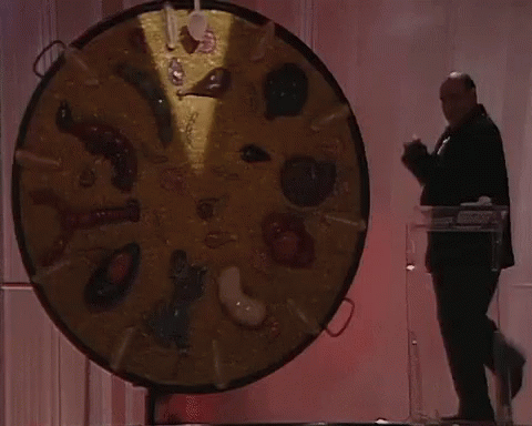 A Man Stands In Front Of A Large Circular Display Of Food Items GIF
