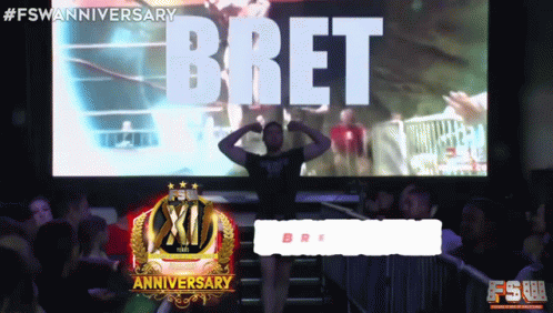 A Man Stands In Front Of A Large Screen That Says Bret On It GIF