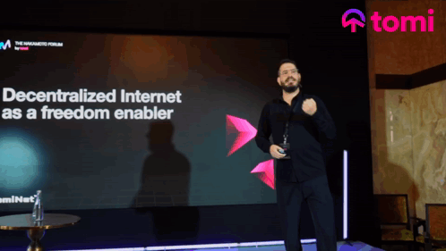 A Man Stands In Front Of A Large Screen That Says " Decentralized Internet As A Freedom Enabler " GIF