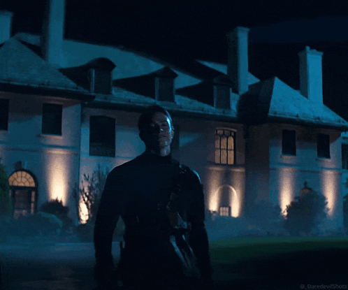 A Man Stands In Front Of A Large White Building At Night With The Words Daredevilshots Below Him GIF