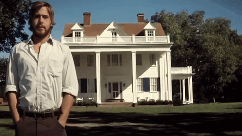 A Man Stands In Front Of A Large White House With His Hands In His Pockets GIF