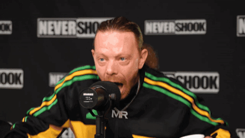 A Man Stands In Front Of A Microphone In Front Of A Sign That Says Never Shook GIF